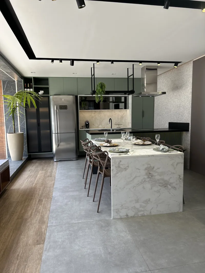 Cozinha exposta no showroom, com ilha em pedra clara e armários verdes